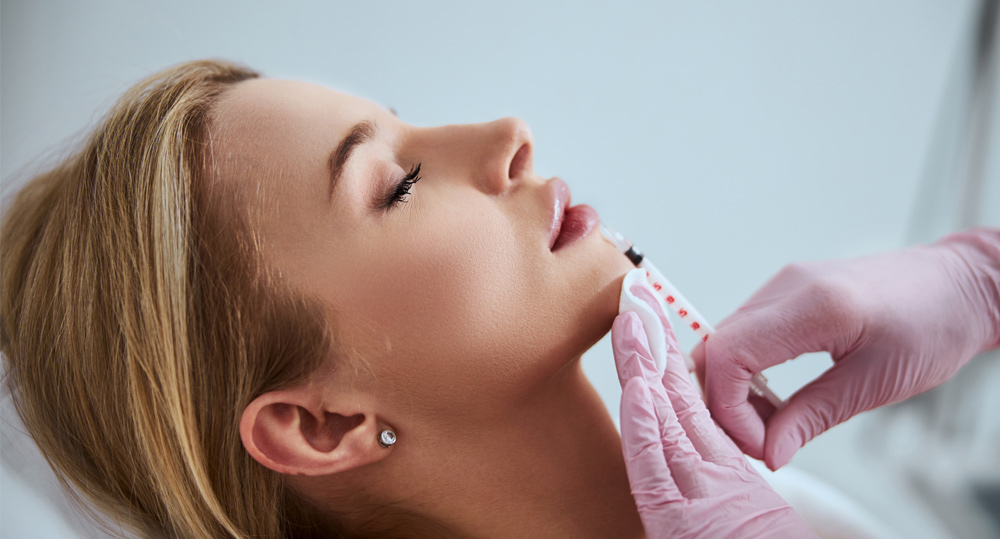 Professional cosmetologist injecting a dermal filler into the patient lips
