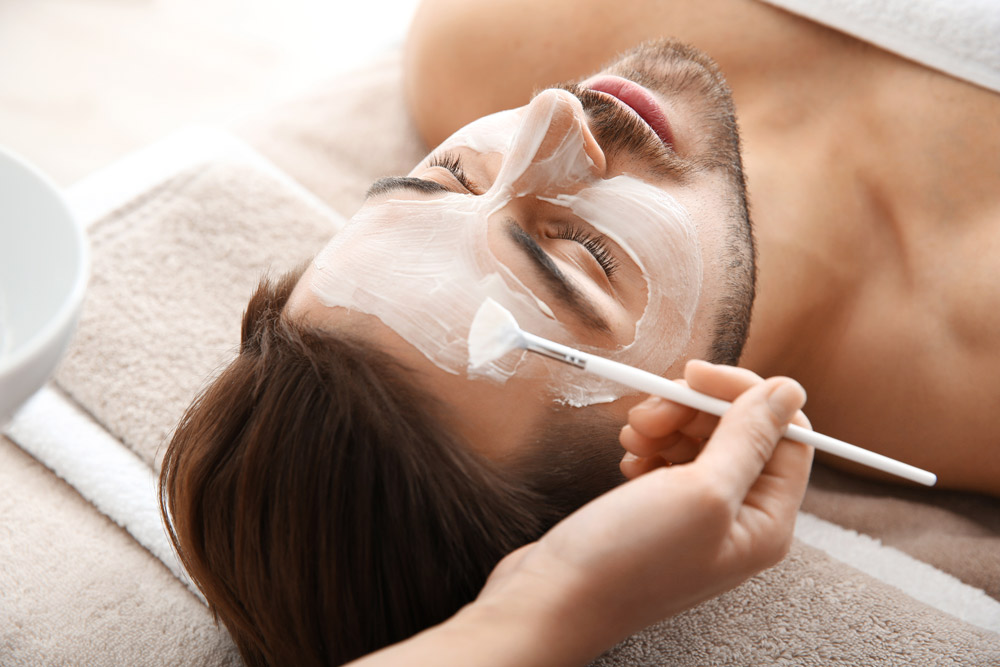 Cosmetologist applying mask on client's face in spa salon