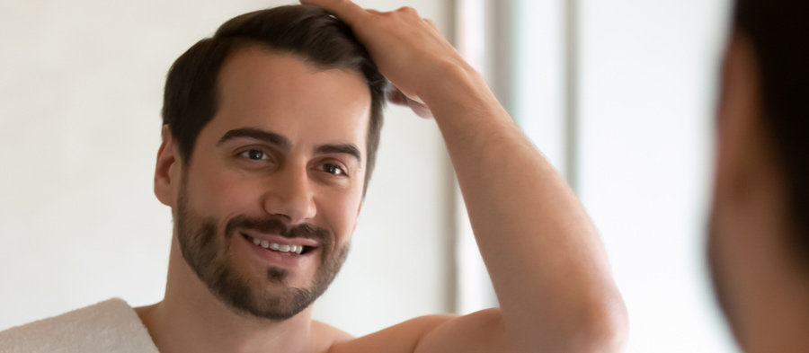 appy millennial handsome man in towel look in mirror in bathroom at home get ready in morning. Smiling young male style hair make hairdo prepare with procedures in bath.