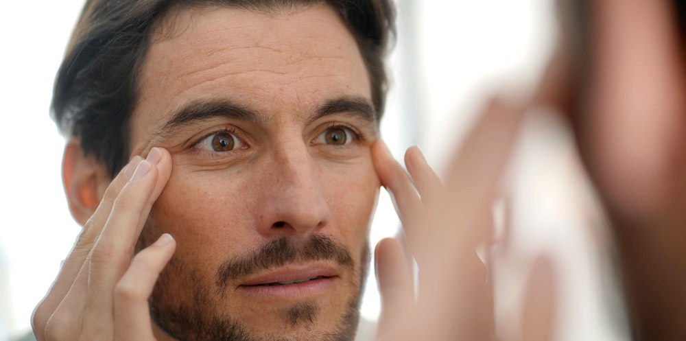 Handsome man checking wrinkles in mirror at home