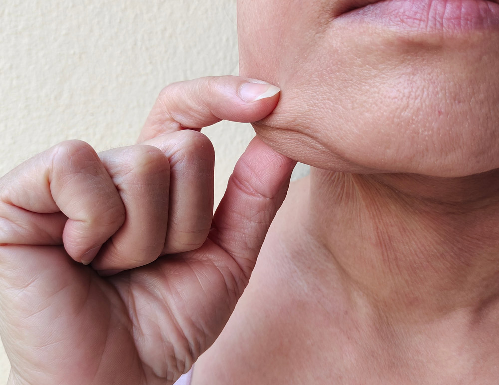 close up the fingers squeezing flabbiness skin beside the chin, problem flabby and hanging skin concept health care.