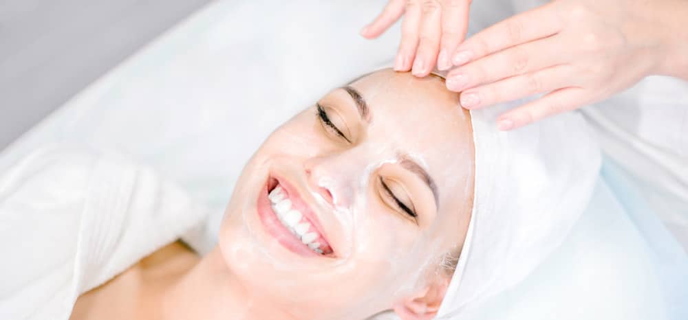 Beautician makes facial massage with mask. Beautiful smiling girl on spa procedure. Facial care.